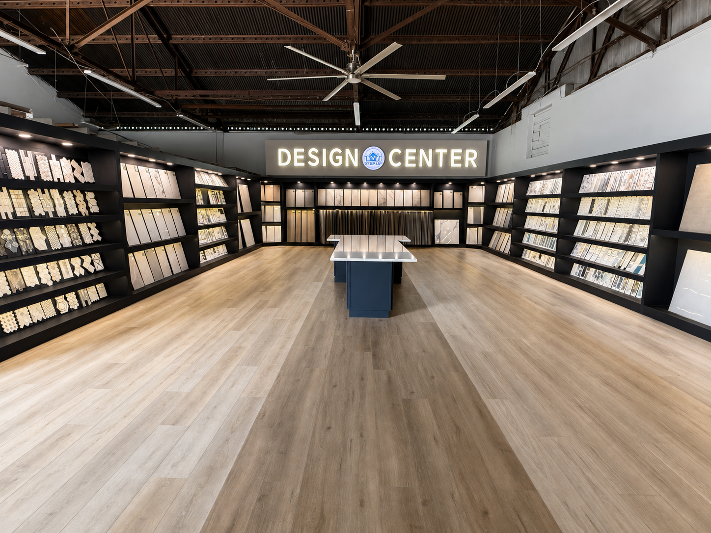 Spacious flooring showroom with wood samples on walls, central table, and a “DESIGN CENTER” sign