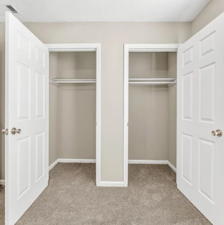 Empty beige bedroom closet with double doors open and carpeted floor