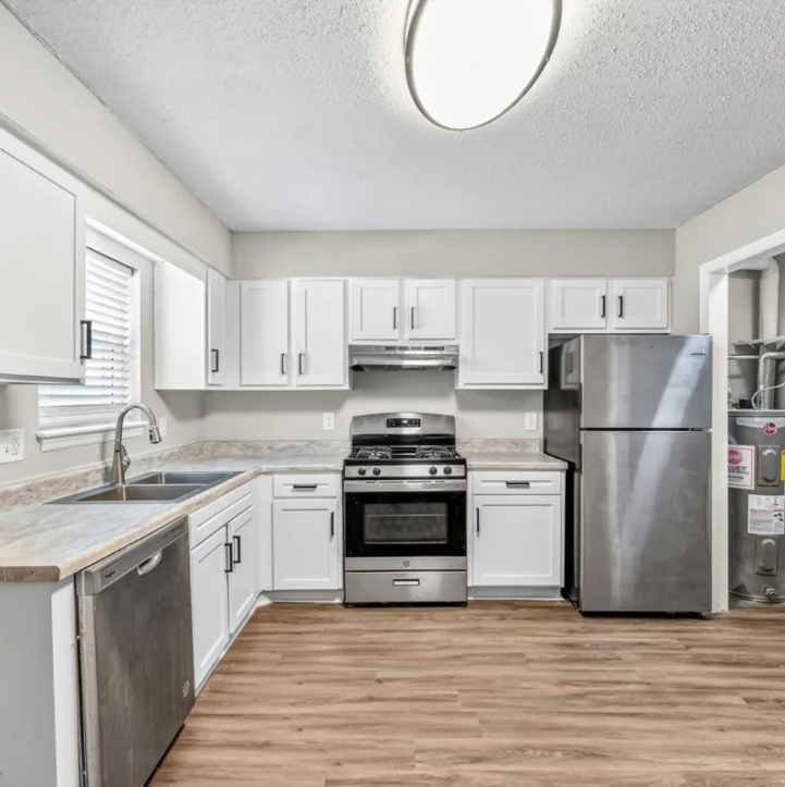 Bright white kitchen with stainless steel appliances, wood floors, and an oval ceiling light.