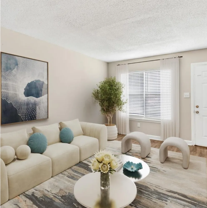 Bright beige living room with cream sofa, round coffee table, abstract wall art, and a window with blinds.