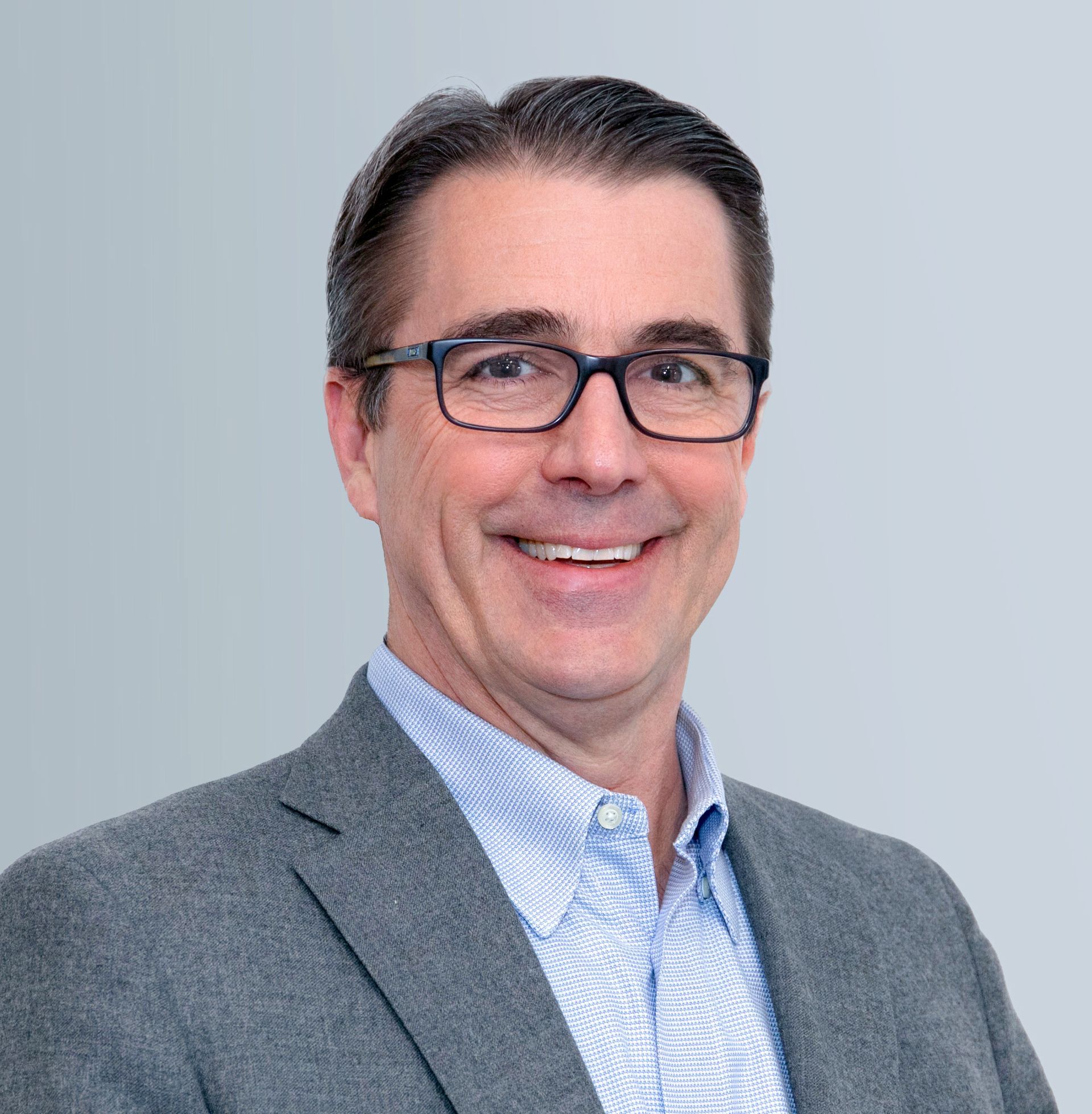 A man wearing glasses and a suit is smiling for the camera.