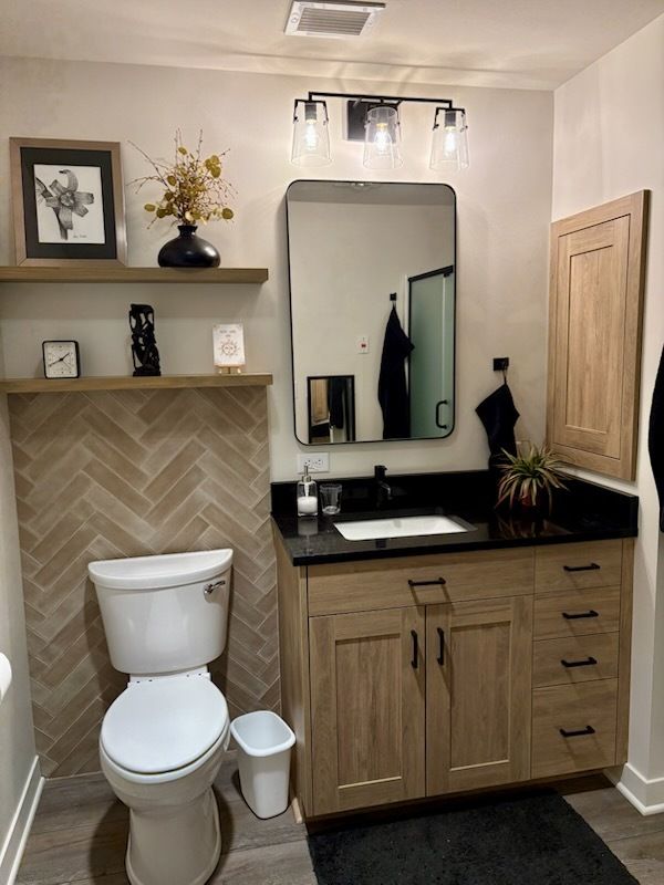 Bathroom with wooden vanity, black countertop, herringbone tile, and floating shelves with decor.