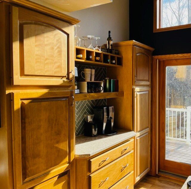Wooden kitchen cabinets with a coffee station. Cabinets are light brown, and include a coffee machine, and wine rack.