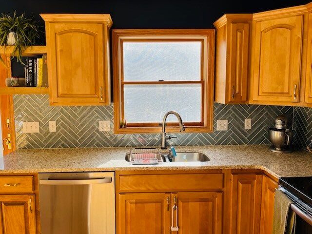 Kitchen with wooden cabinets, backsplash, sink, window, and stainless steel appliances.
