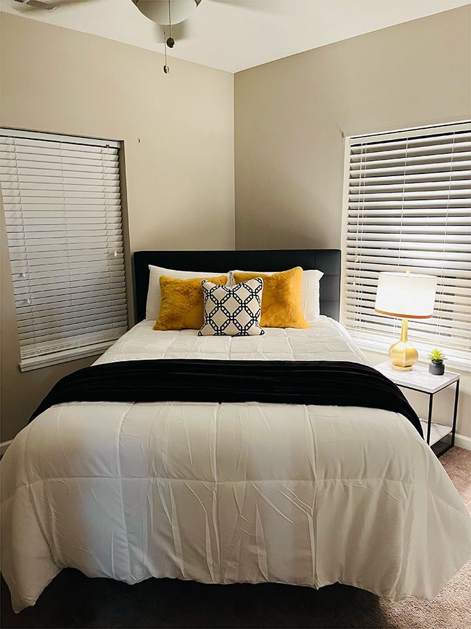 A bedroom with a bed , nightstand , lamp and blinds.