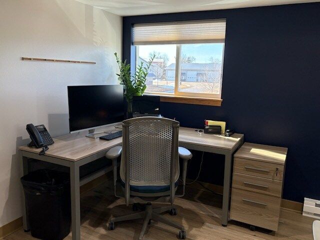 Office corner with desk, chair, computer, and a filing cabinet next to a window with a blue wall.