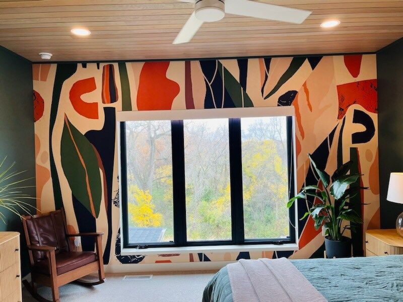 Bedroom with abstract mural, large window, rocking chair, and plants.