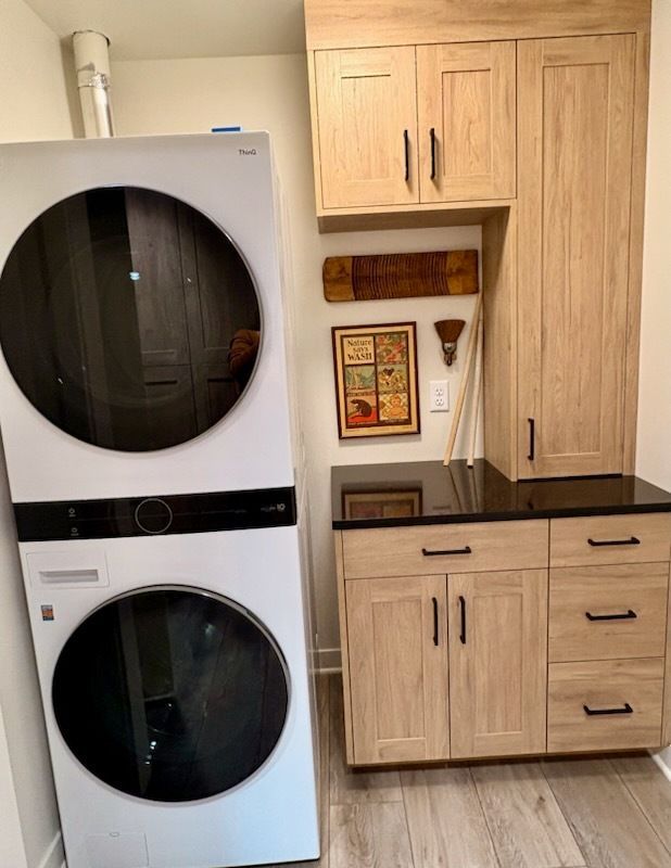 Stacked white washer and dryer next to light wood cabinets in a laundry room.
