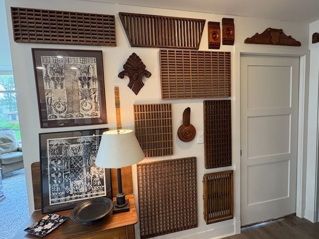 Wall with wooden vent covers and framed photos, a lamp, and a closed white door.