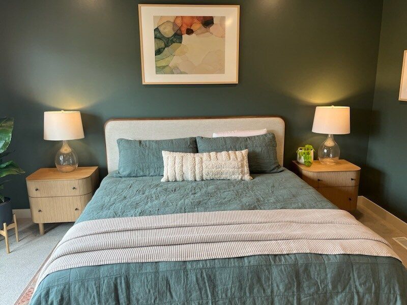 Bedroom with a bed, nightstands, lamps, and artwork; teal bedding, green walls.