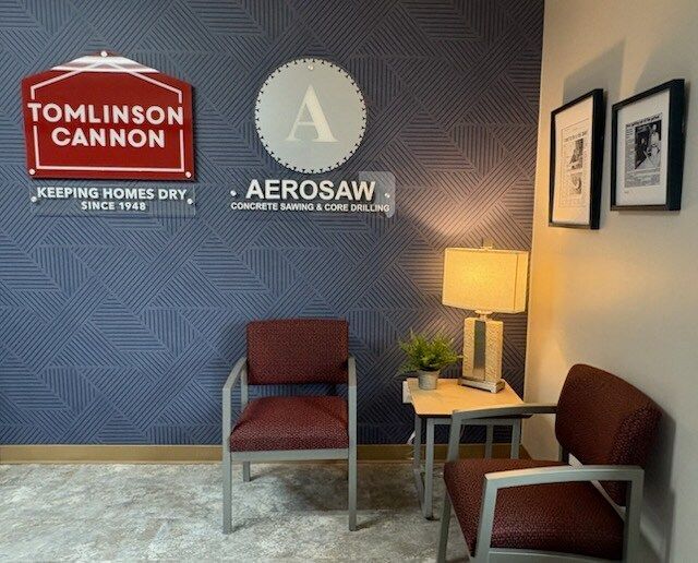 Waiting area with company logos, red chairs, side table, lamp, and framed art against patterned blue wall.