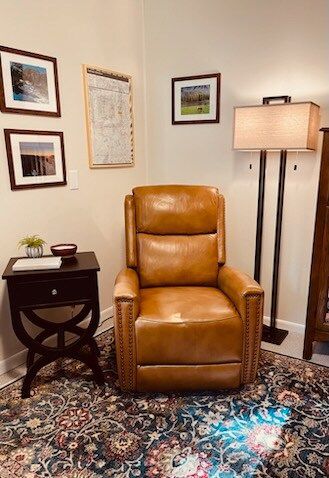 Cozy reading nook: brown leather recliner, side table, framed art, floor lamp, and patterned rug.