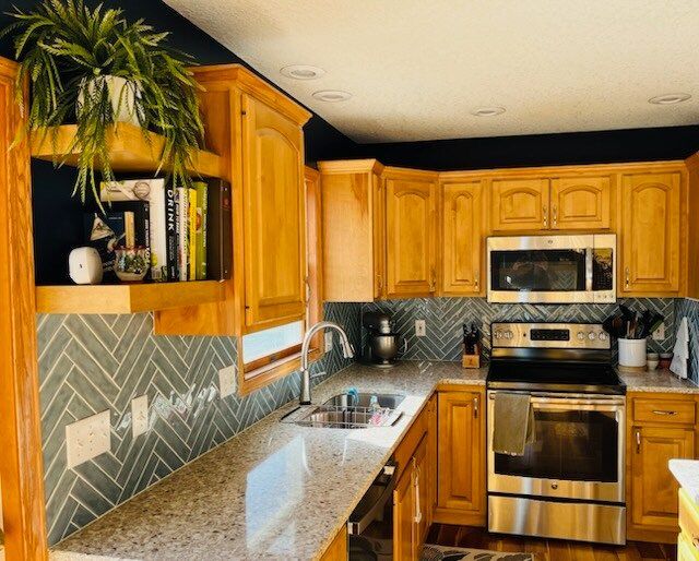 Kitchen with wooden cabinets, stainless steel appliances, and a gray herringbone tile backsplash.