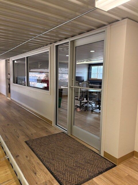 Office hallway with wooden floor, glass door, windows, and doormat.