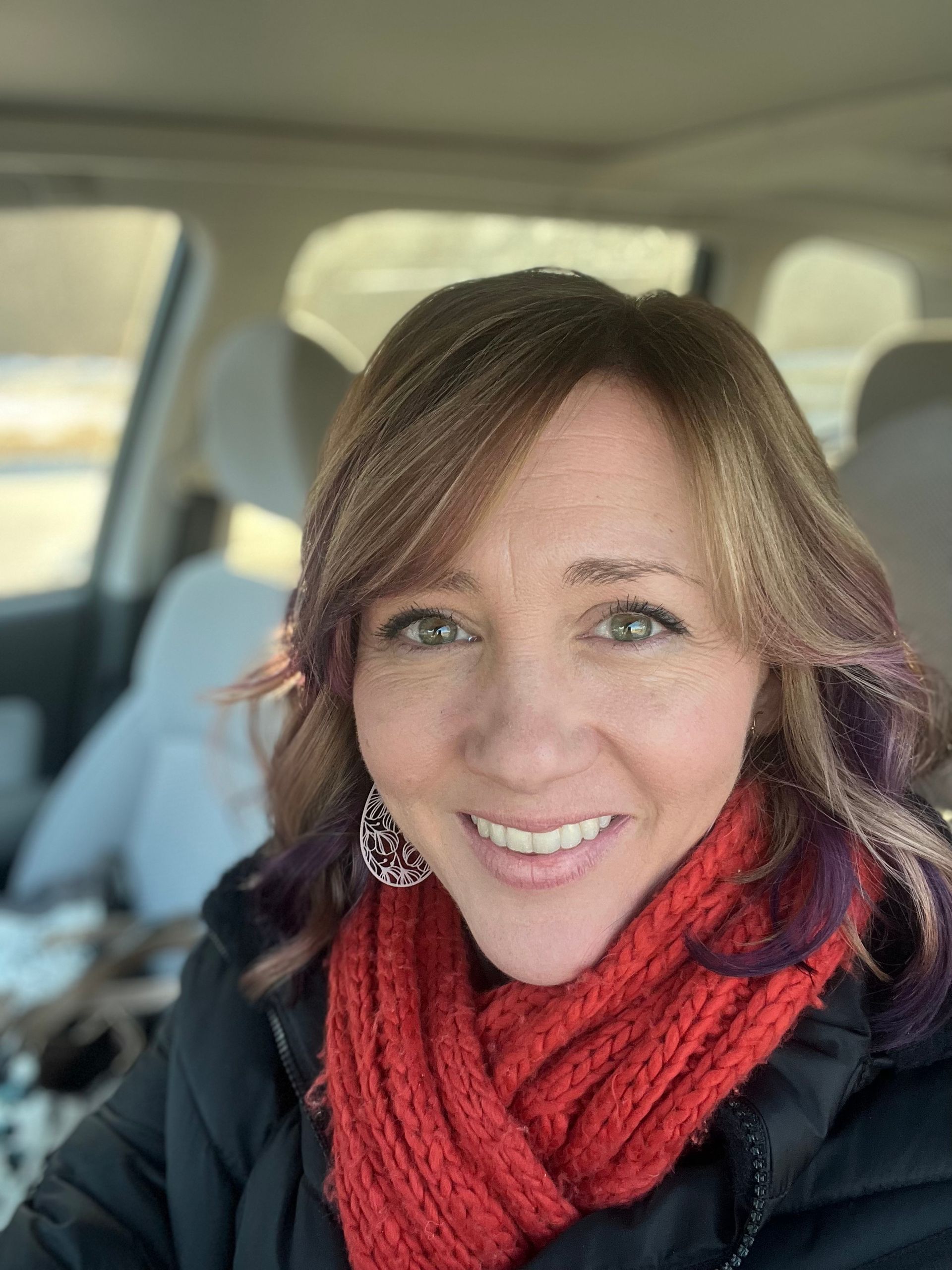 Woman in car smiling, wearing a red scarf.