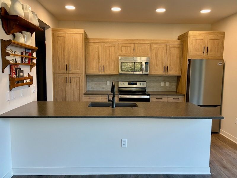 Modern kitchen with light wood cabinets, dark countertop island, stainless steel appliances.