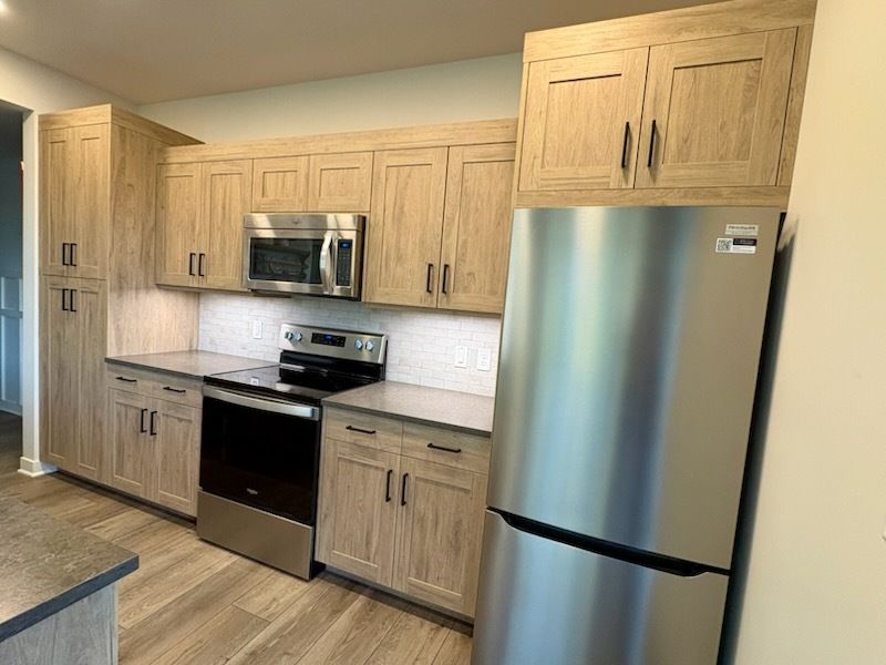 Kitchen with light wood cabinets, stainless steel appliances, and white tile backsplash.