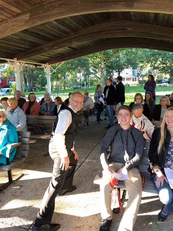 A group of people are sitting on benches under a canopy in a park.