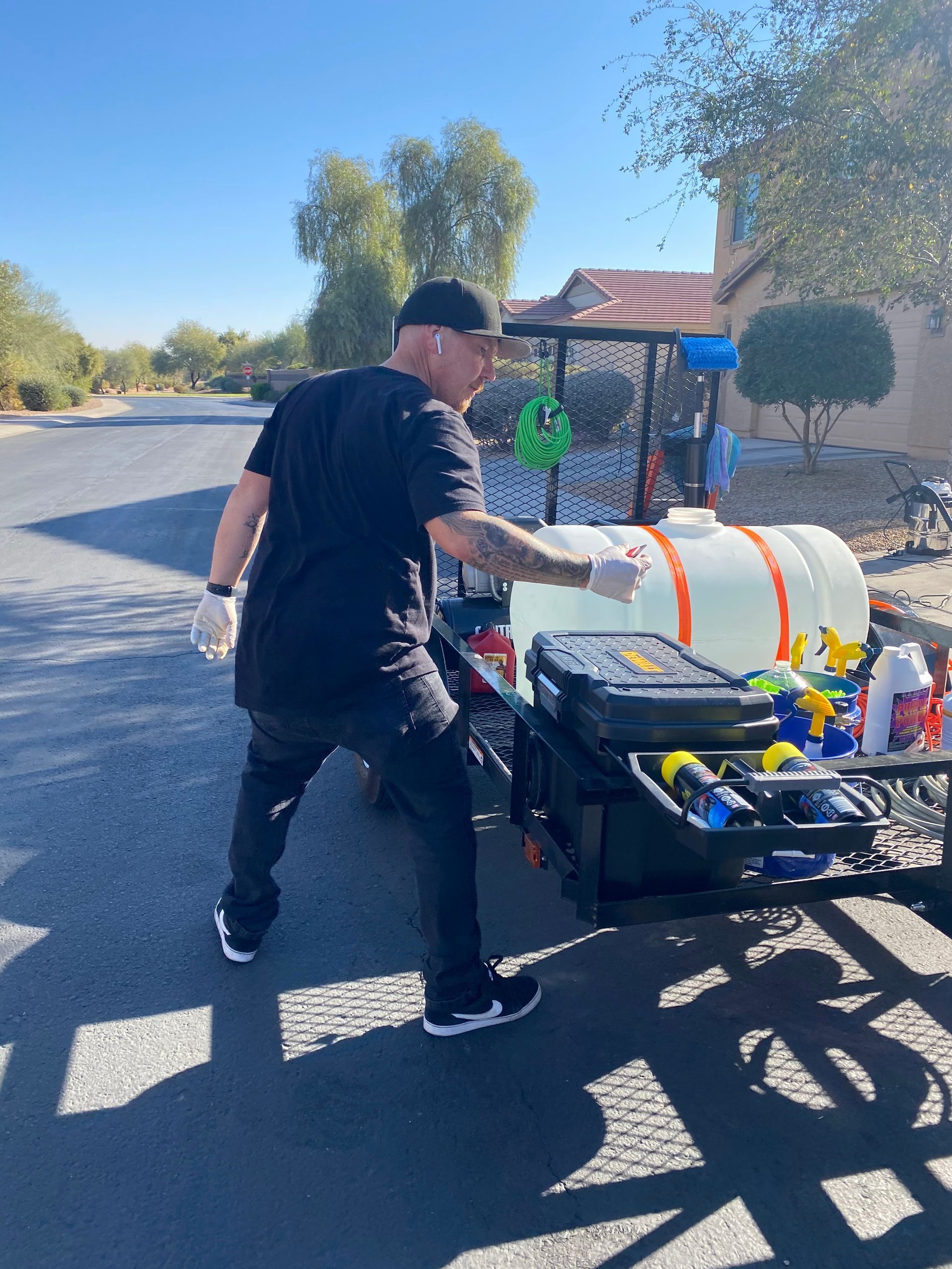 Man in black clothes with cleaning equipment on a trailer outside; pointing.