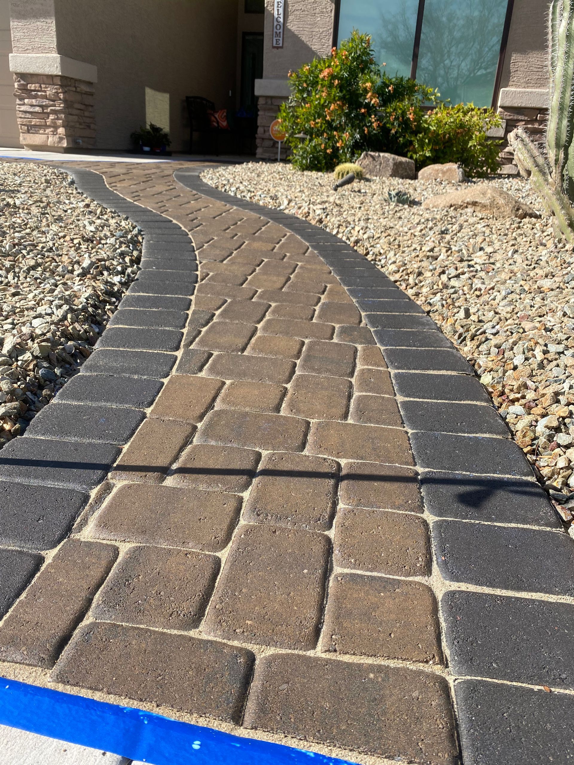 Brick pathway leading to a house, flanked by gravel and landscaping, dark border.