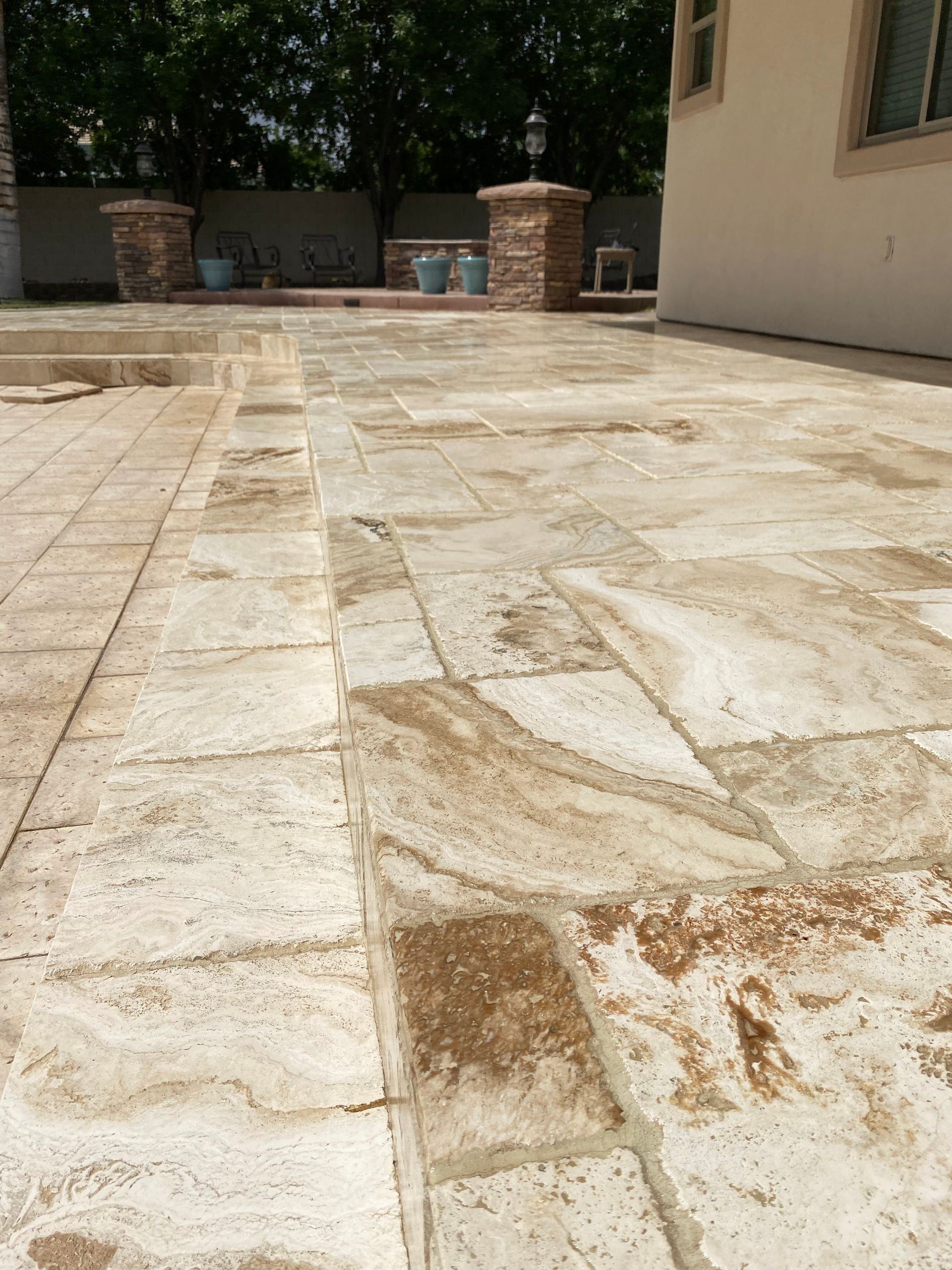 Stone patio with rectangular tiles. Some tiles have brown dirt and debris on them. Brick pillars in background.