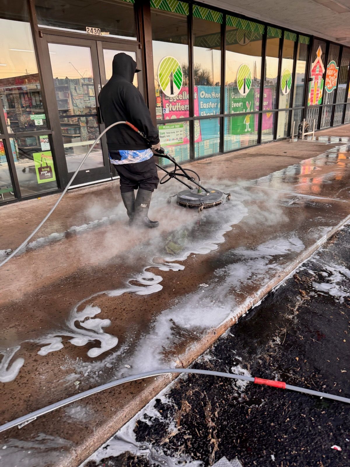 Person power washing a sidewalk outside a store, creating suds.