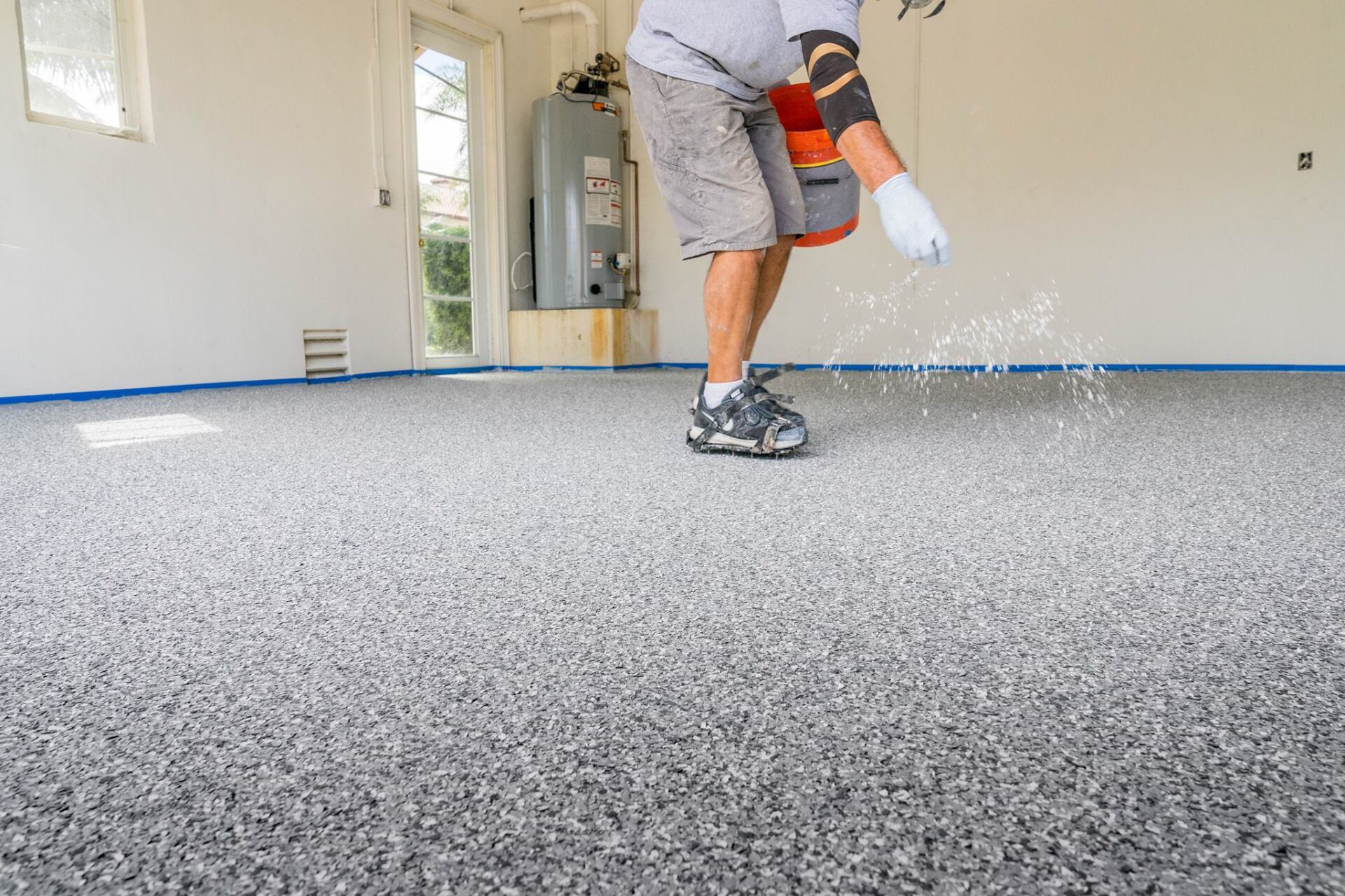 Worker spraying coating on a garage floor with an orange sprayer