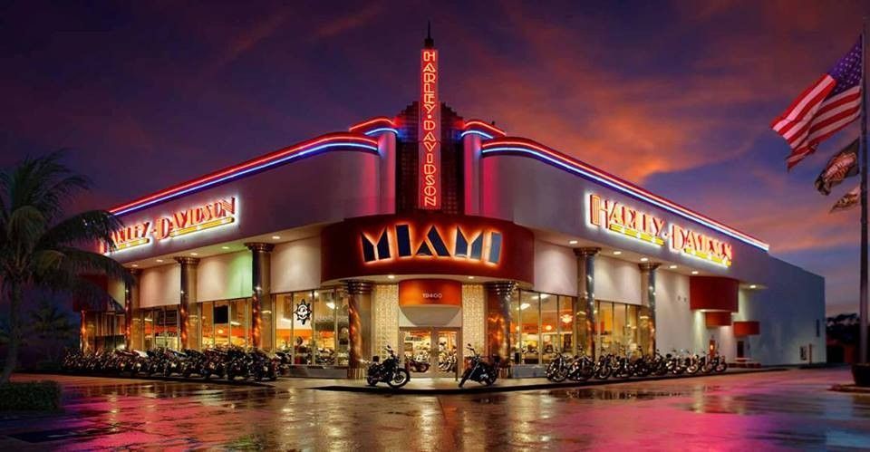 Neon-lit Miami restaurant at dusk with red signage, palm trees, and parked cars outside