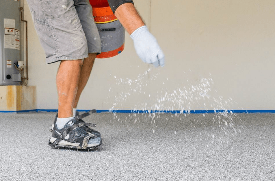 Worker spreading liquid coating on a gray floor with a gloved hand.