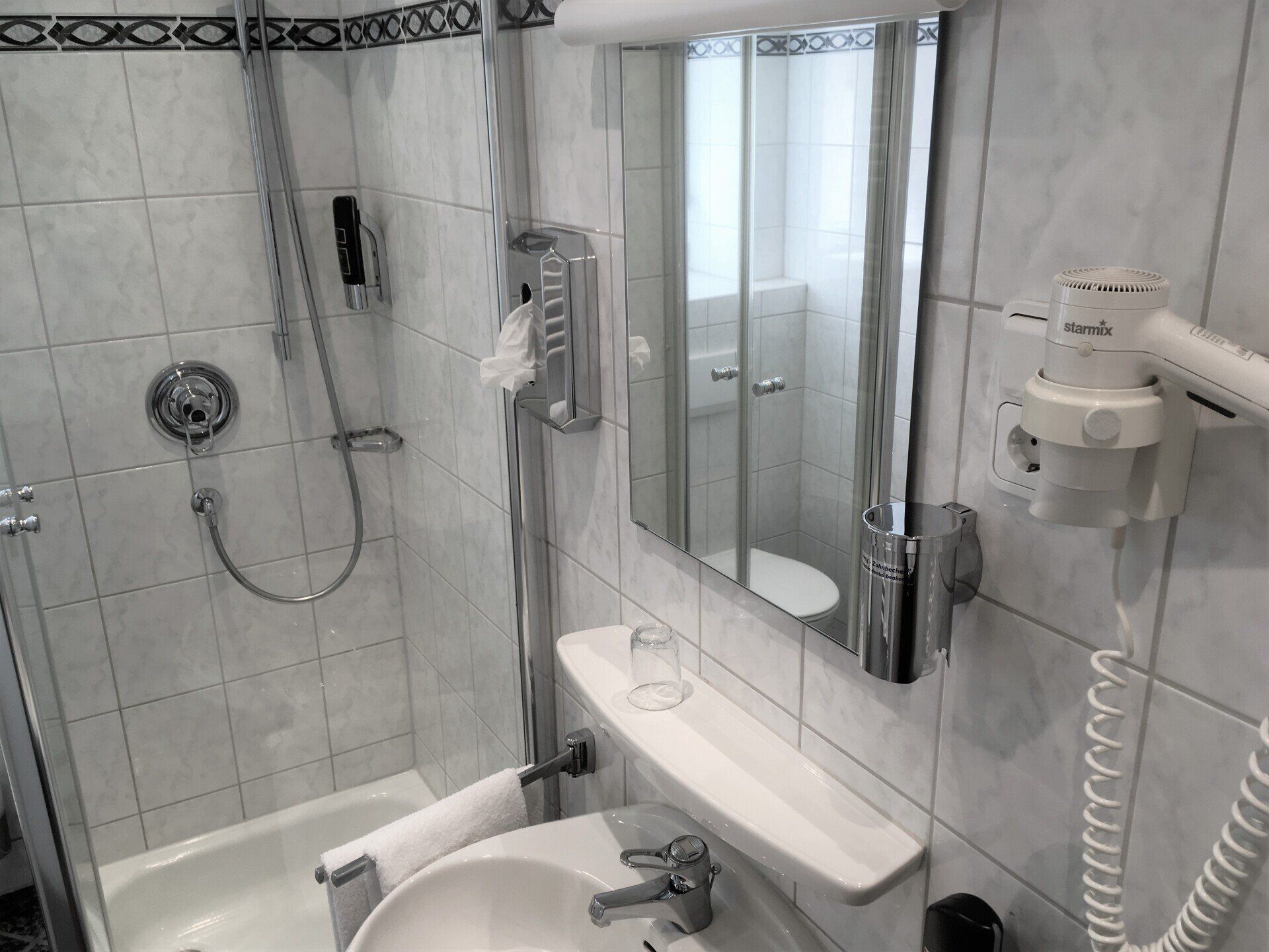 Ein Badezimmer mit Waschbecken, Dusche, Spiegel und Haartrockner.