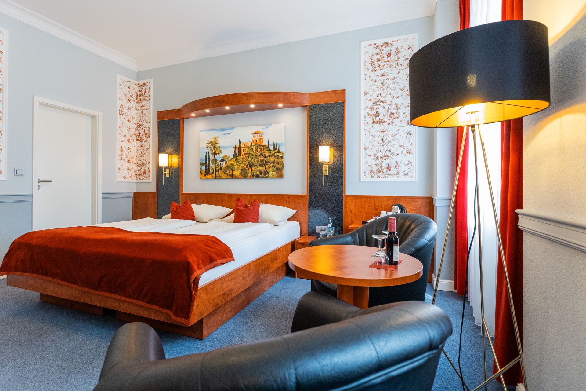 Ein Hotelzimmer mit großem Bett, Stuhl, Tisch und Lampe.