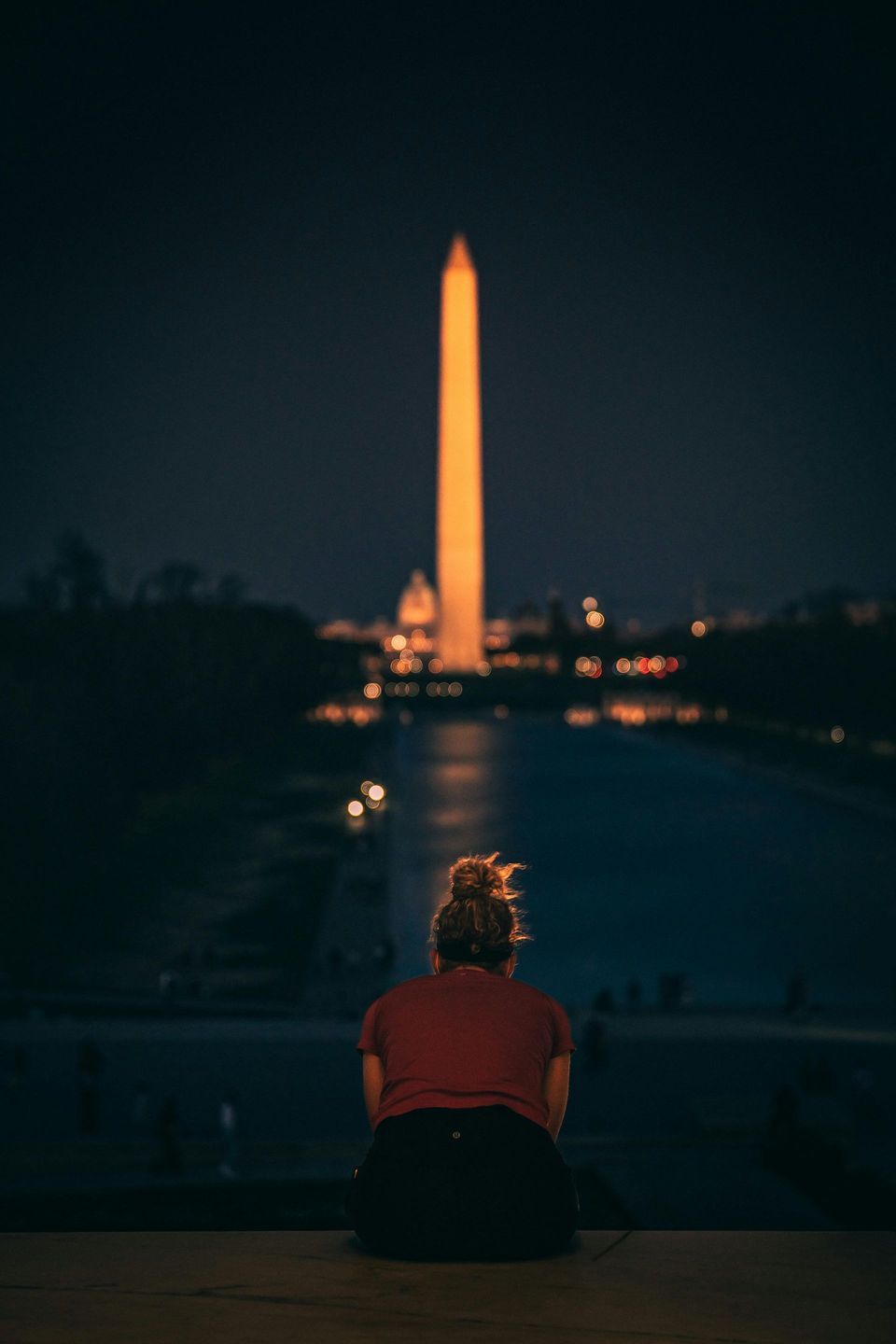 Person in red sits overlooking the illuminated Washington Monument at night