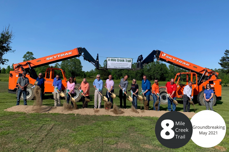 Group posing with orange excavators at 8 Mile Creek Trail groundbreaking, May 2021
