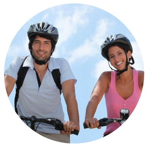 Two cyclists smiling on a bright day, viewed from below against a blue sky.