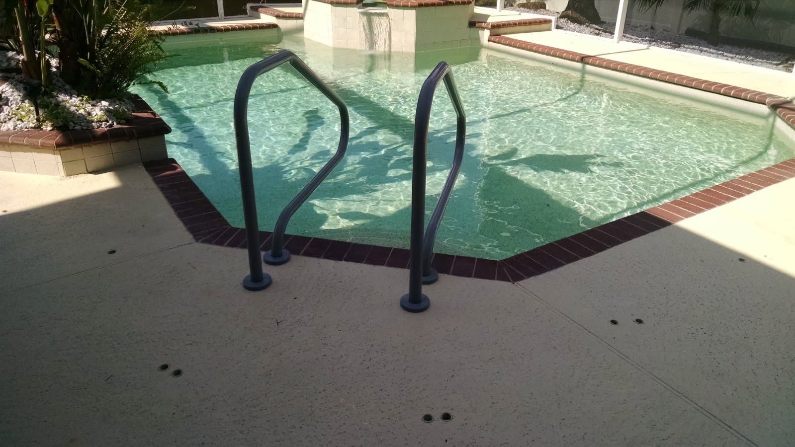 Pool with dark ladder and surrounding brick, sunny day.