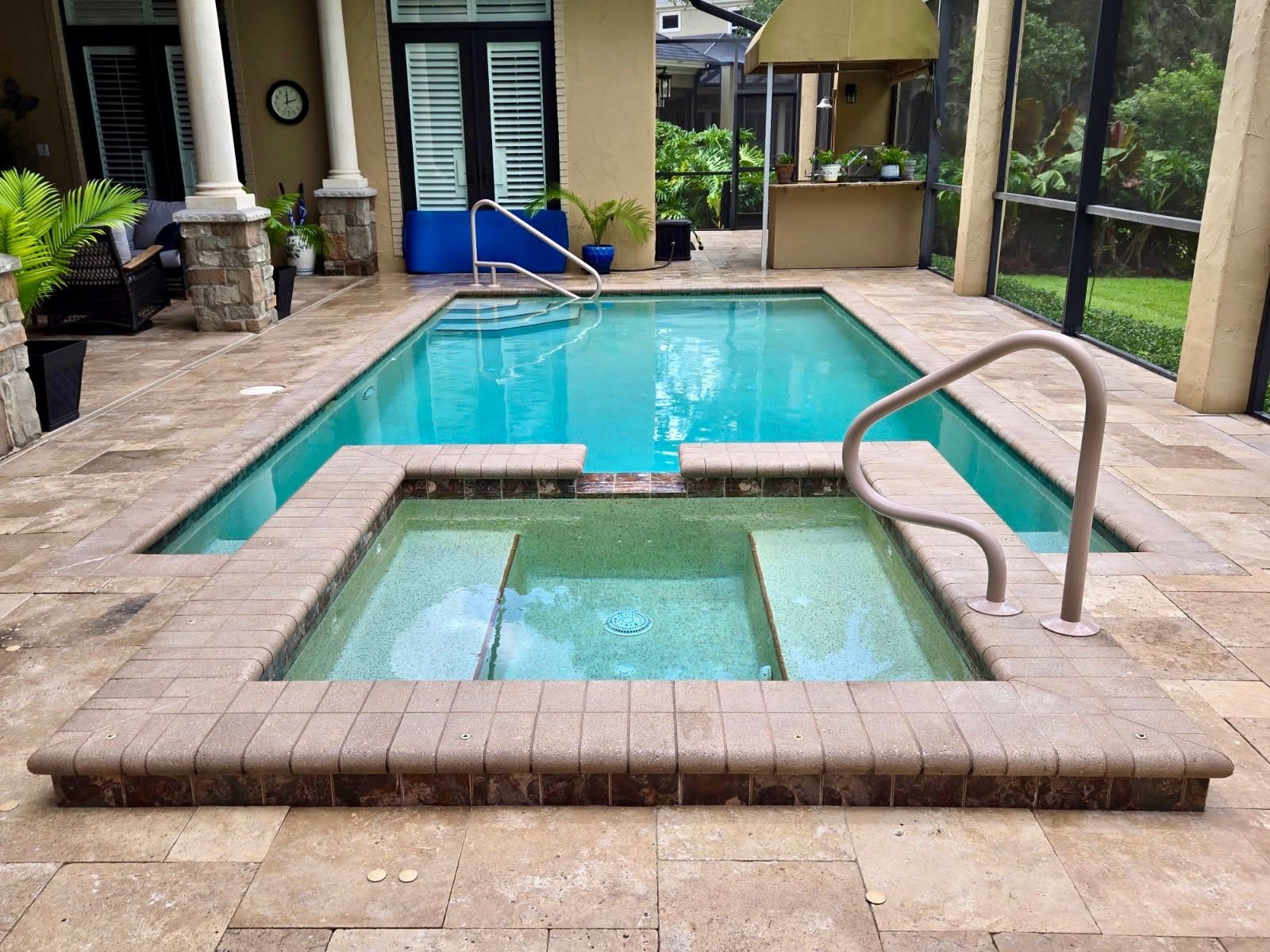 Swimming pool and jacuzzi surrounded by tile patio, enclosed in a screened-in area.