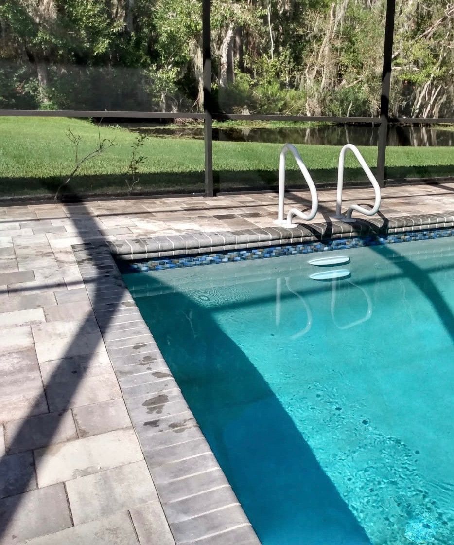 Swimming pool with a blue interior, white handrails, and a stone patio.