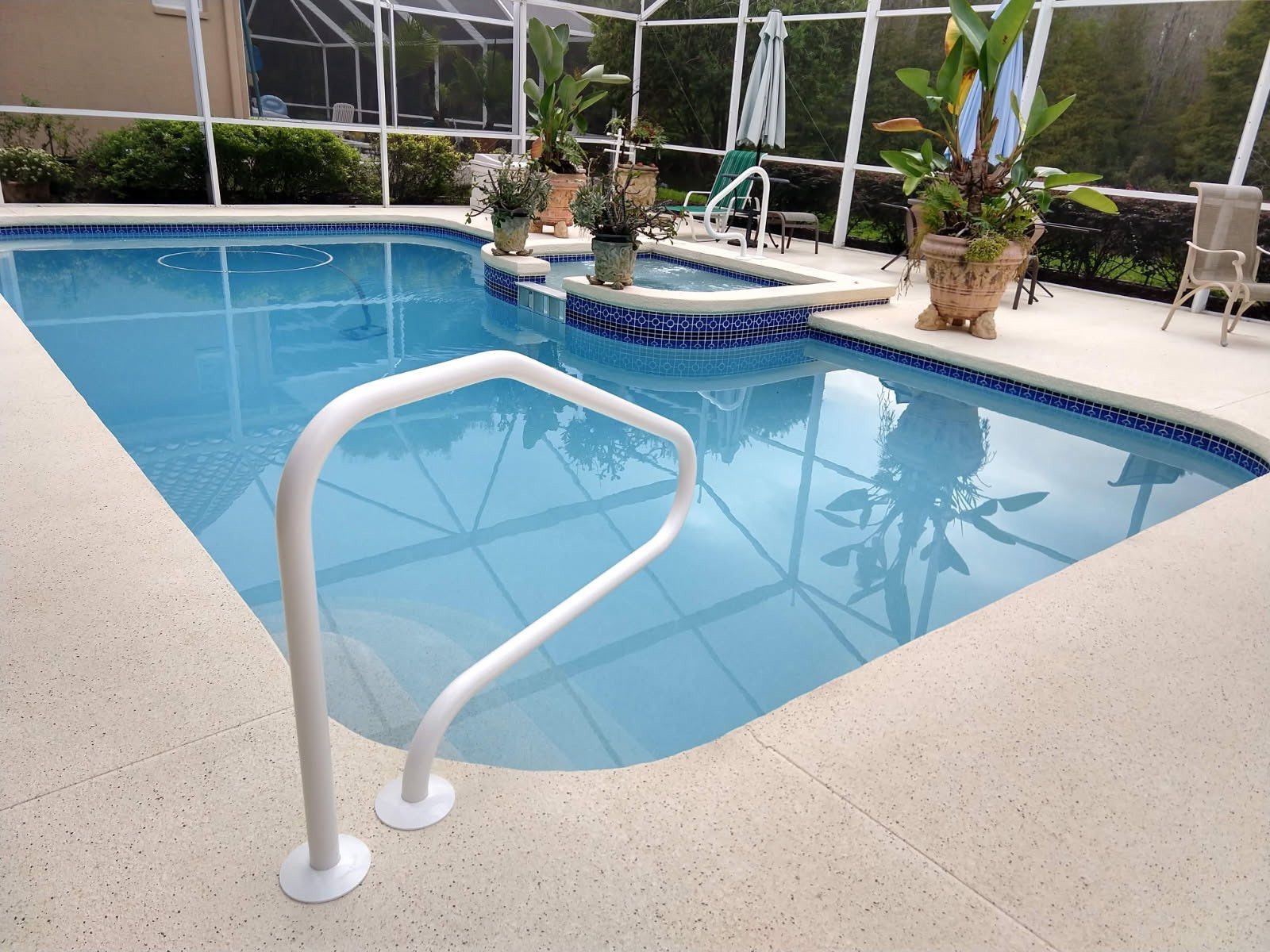 A swimming pool with a white handrail and potted plants on the deck.