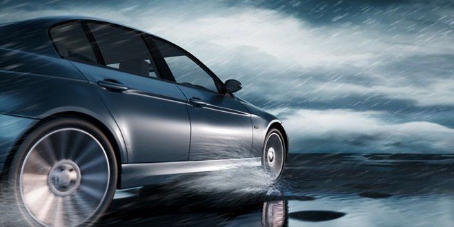 Sleek silver car speeding across a wet road under a stormy sky