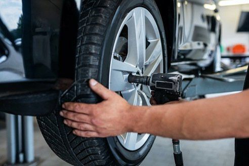 Mechanic tightening a car tire with a power wrench in a garage