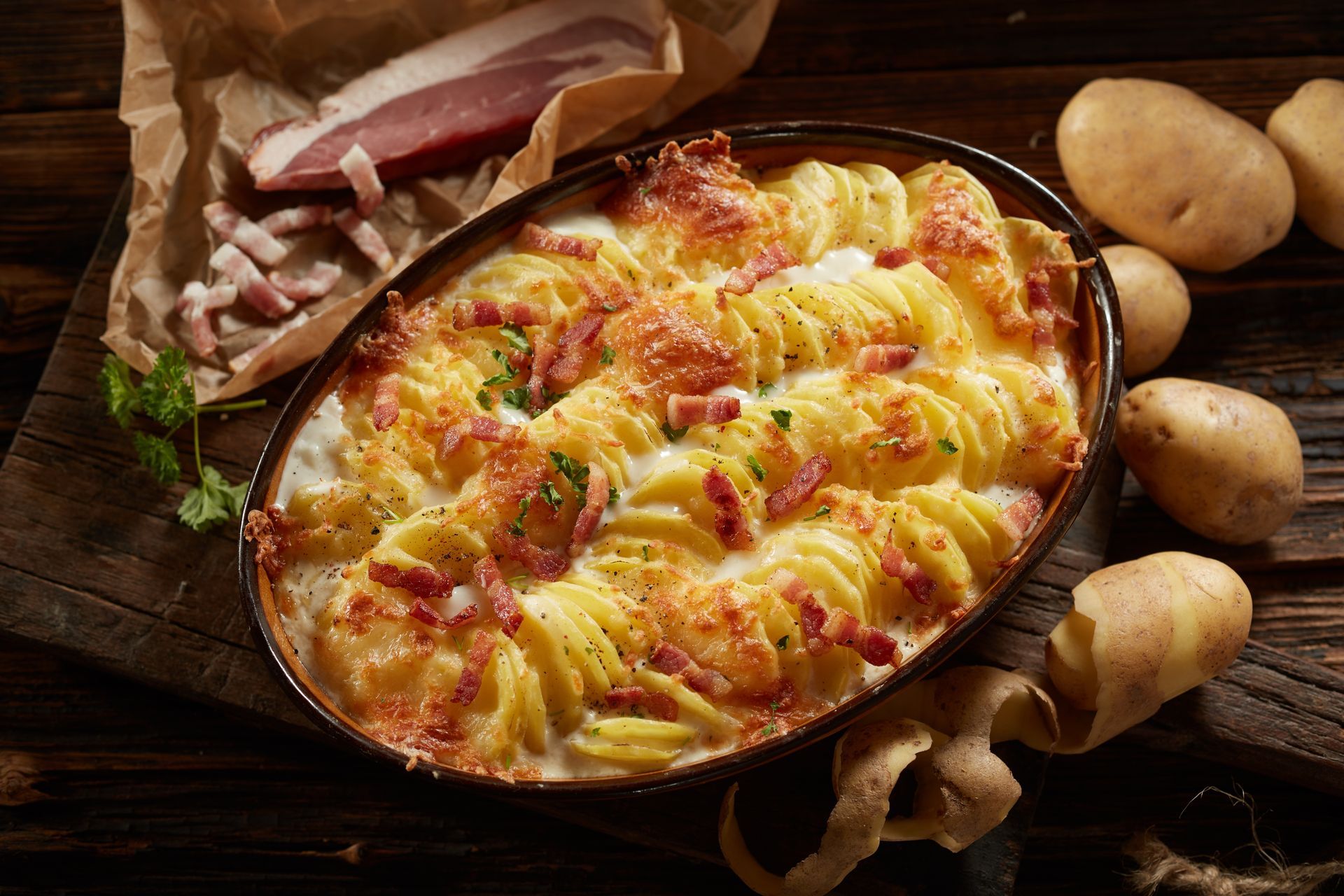 A casserole dish filled with potatoes and bacon on a wooden table.