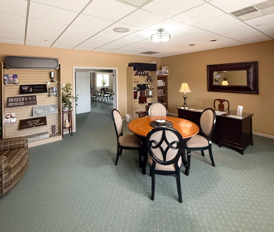 A well-lit room with a round table and chairs.  Other furnishings include a display, a desk and a mirror.