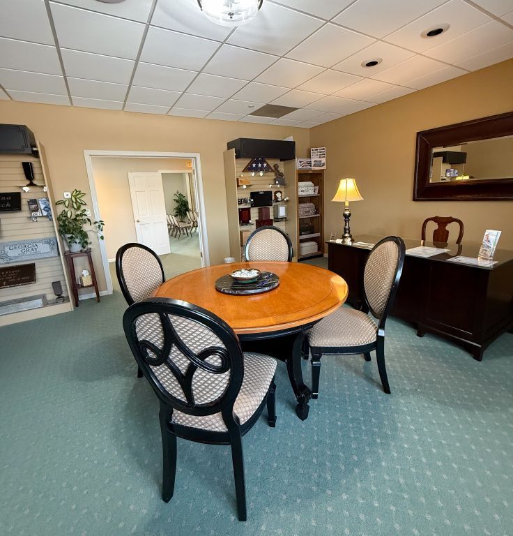 A consultation room with a round table, chairs, and a desk; light blue carpet.