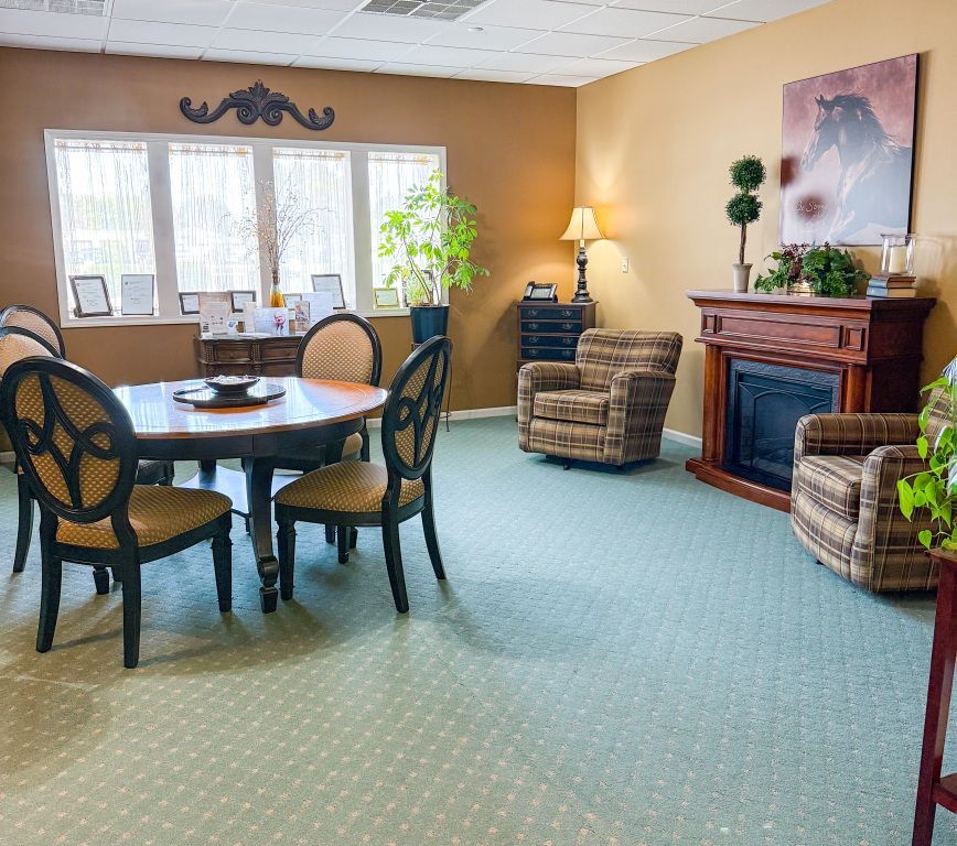 Room with round table, chairs, fireplace, and two armchairs; light green carpet; beige and brown walls.