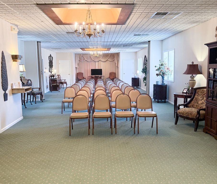Empty memorial room, chairs arranged for a service, green carpet, chandelier, and a stage.