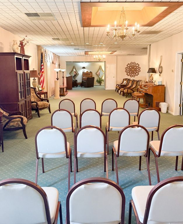 Rows of chairs face a room with a casket area, for a funeral or memorial service.