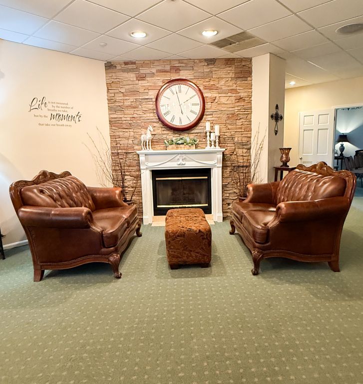 Living room with fireplace, leather chairs, and ottoman. Stone wall and clock.