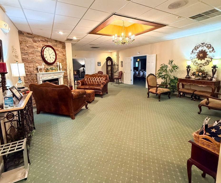Spacious waiting room, decorated in warm tones, with seating, clock, fireplace and green carpet.