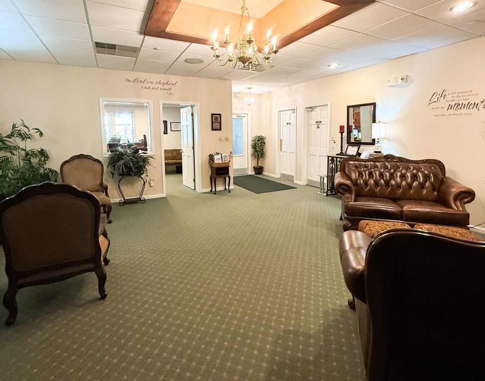 Waiting room with seating, chandelier, and doors. Green carpet, tan walls, and brown leather furniture.