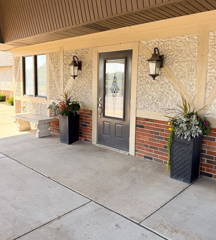 Entrance with a black door, planters, and sconces on a textured wall and brick trim under an overhang.